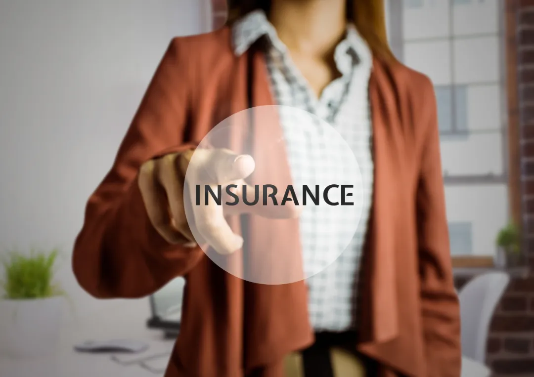 72748565_m A professional woman in a blazer points towards the word "INSURANCE" in a circular overlay, set in a modern office environment.